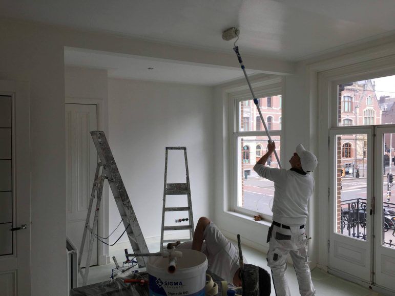 Schilder van Wolkers rolt een plafond in een lichte woonkamer